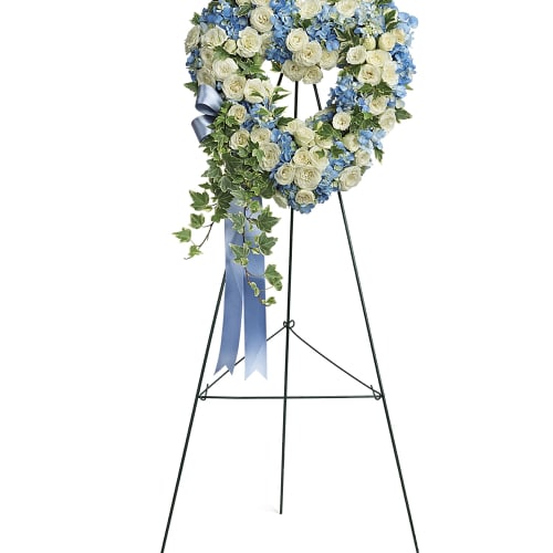 Heart-shaped floral wreath on a stand with blue and white flowers