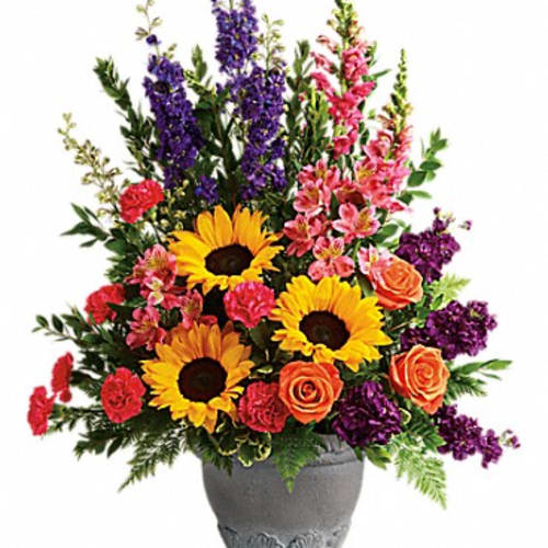 Colorful bouquet with sunflowers, roses, and purple spikes in a gray vase