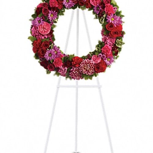 Circular floral wreath on a white easel with red and pink flowers