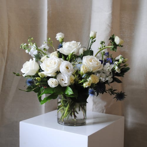 White rose bouquet in a clear glass vase with blue accents