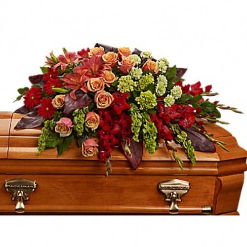 Floral casket spray with red, peach, and green blooms on a wooden casket