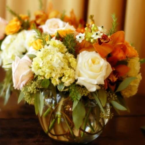 Mixed bouquet of white roses, yellow blooms, and orange flowers in a glass vase