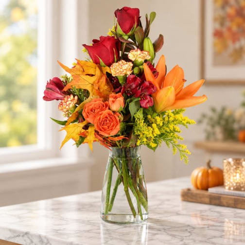 Autumn bouquet of red roses, orange lilies, and yellow filler in a glass vase