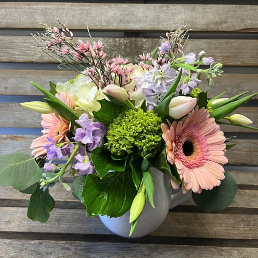 Mixed bouquet with pink gerbera daisies and lavender blooms in a white vase