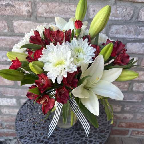 Red and white mixed flower bouquet in a clear glass vase with a striped ribbon bow