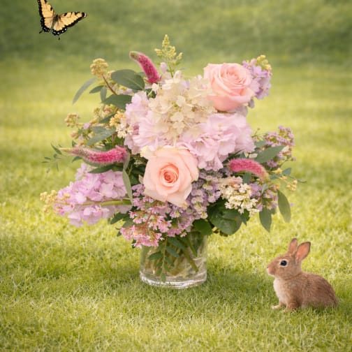 Pink rose bouquet in a glass vase with a butterfly and rabbit nearby