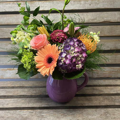 Mixed bouquet in a purple pitcher vase with pink, orange, and purple blooms
