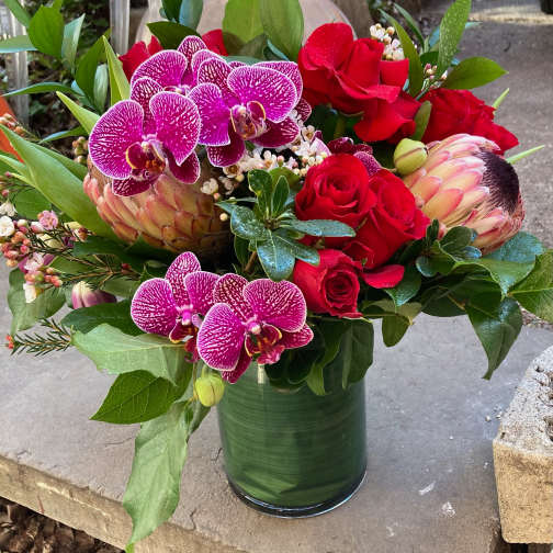 Bouquet of red roses and purple orchids in a green glass vase