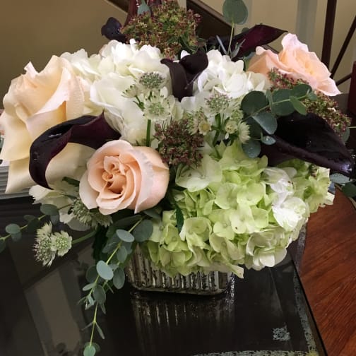 Mixed bouquet with pale roses, white hydrangeas, and dark calla lilies in a square vase