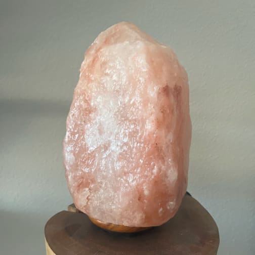 Pink salt lamp on a wooden base against a plain wall