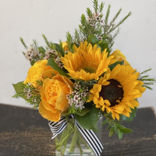 Yellow sunflower and rose bouquet in a glass vase with a striped ribbon