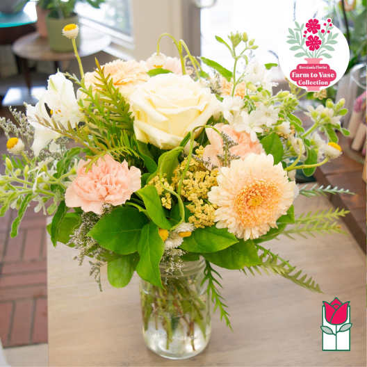 Mixed bouquet of cream, peach, and white flowers in a glass vase