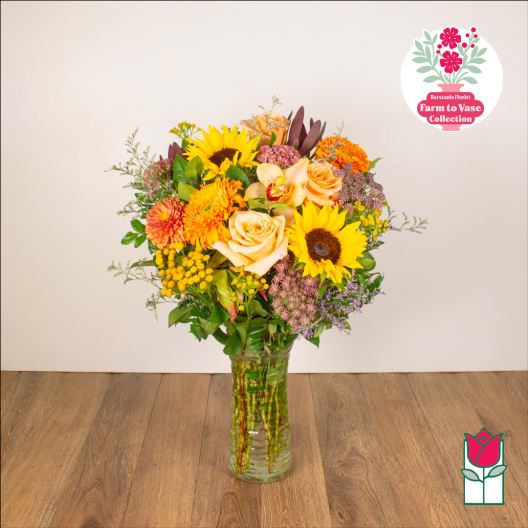 Mixed bouquet of sunflowers, roses, and orange blooms in a glass vase
