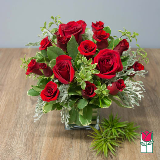 Red roses arranged in a square glass vase with mixed greenery