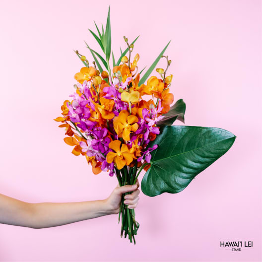 Handheld bouquet of orange and purple orchids with large tropical leaves