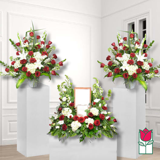 Symmetrical funeral floral display with red roses, white lilies, and white blooms