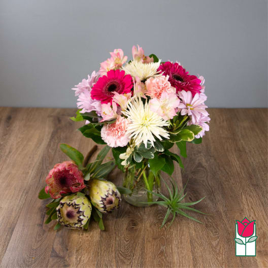 Pink and white mixed bouquet in a glass vase with two protea stems beside it.