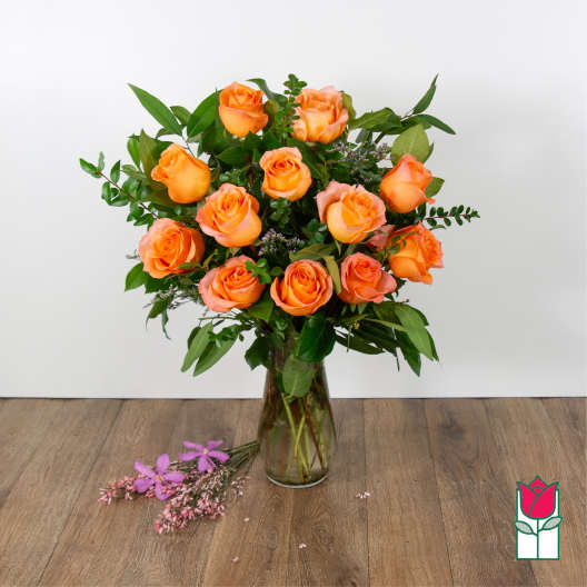 Orange roses arranged in a clear glass vase with greenery.