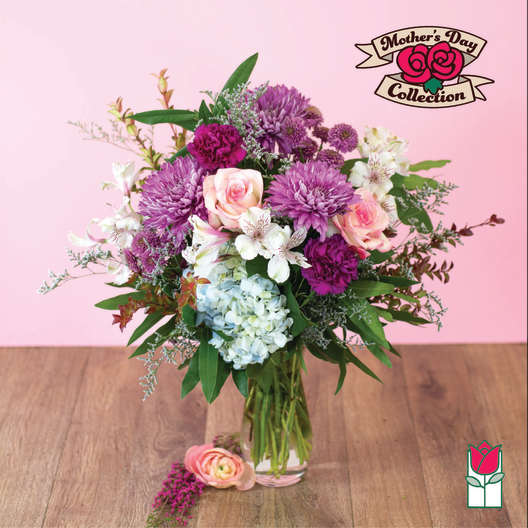 Mixed bouquet of purple mums, pink roses, and blue hydrangea in a clear glass vase
