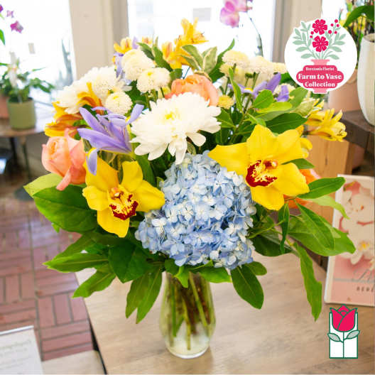 Mixed bouquet in a clear glass vase with blue hydrangea and yellow orchids