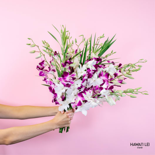 Handheld bouquet of white and purple orchids against a pink background