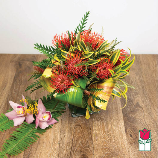 Tropical bouquet with red pincushion blooms and pink orchids in a glass vase