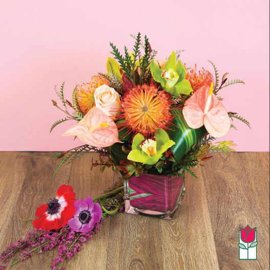 Tropical flower arrangement in a square glass vase with pink accents