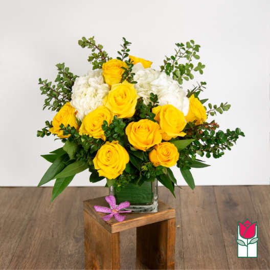 Yellow roses and white hydrangeas in a glass vase with greenery