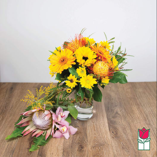 Yellow and orange bouquet in a glass vase with a pink tropical flower arrangement beside it.