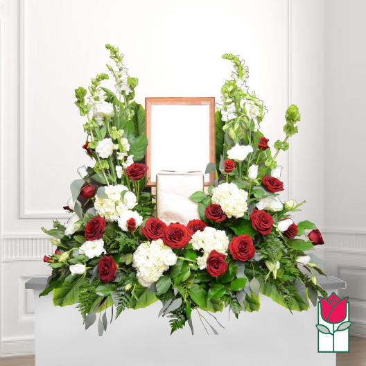 Symmetrical floral funeral arrangement with red roses and white blooms around a framed center