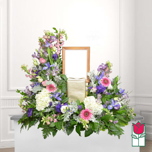 Large floral funeral arrangement with pink, purple, and white blooms around a framed center