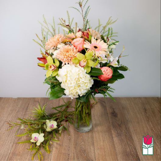 Mixed pastel bouquet in a clear glass vase with orchids and daisies