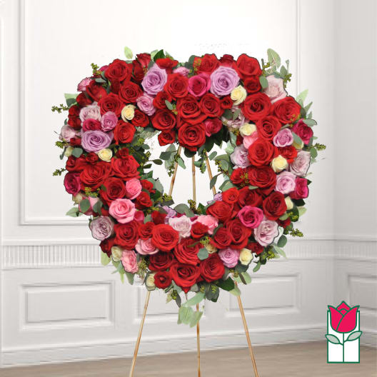 Heart-shaped wreath of red, pink, and lavender roses on a stand