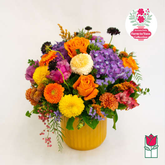 Colorful mixed bouquet in a yellow vase with orange roses and purple blooms