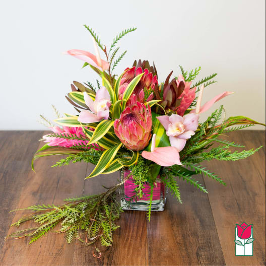 Tropical flower arrangement in a square glass vase with pink blooms