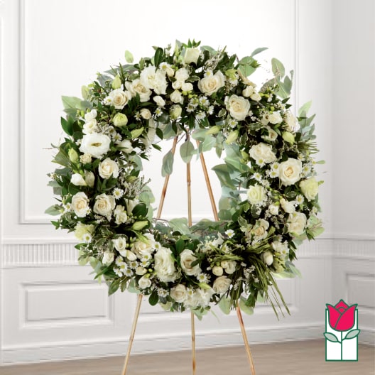 Large white floral wreath on a stand with roses and greenery