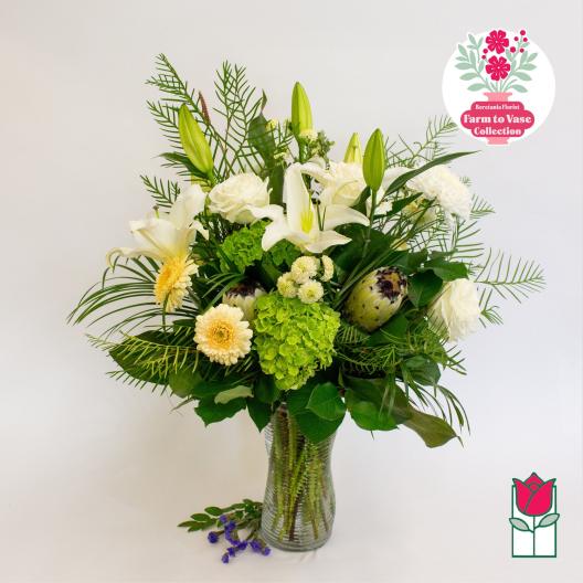 White lilies and cream flowers in a glass vase with green foliage