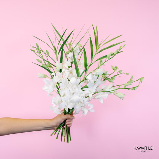 Handheld bouquet of white orchids with long green leaves against a pink background
