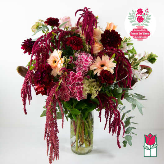 Mixed bouquet of burgundy, pink, and peach flowers in a glass vase