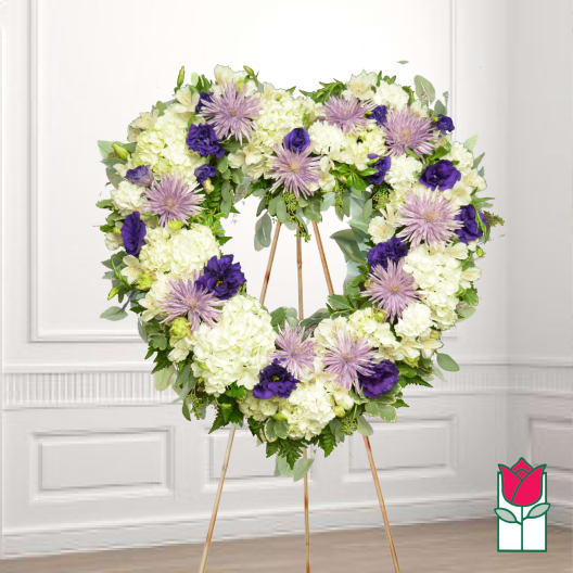 Heart-shaped floral wreath on a stand with white and purple flowers