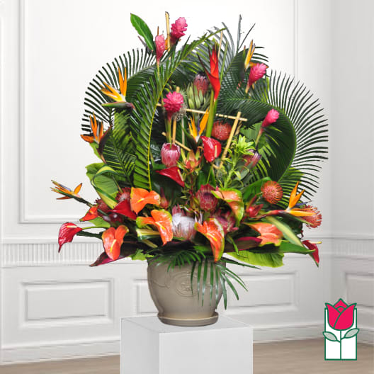 Tropical floral arrangement in a beige urn with orange and pink blooms