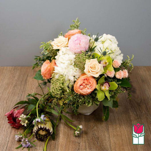 Mixed bouquet in a low white vase with peach, pink, and white blooms