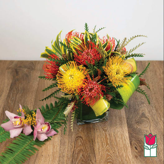 Tropical bouquet with red and yellow pincushion flowers in a square vase