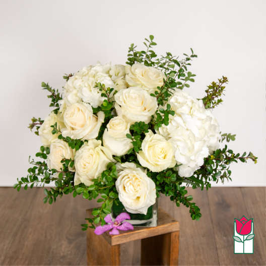 White roses and hydrangeas in a square glass vase with greenery