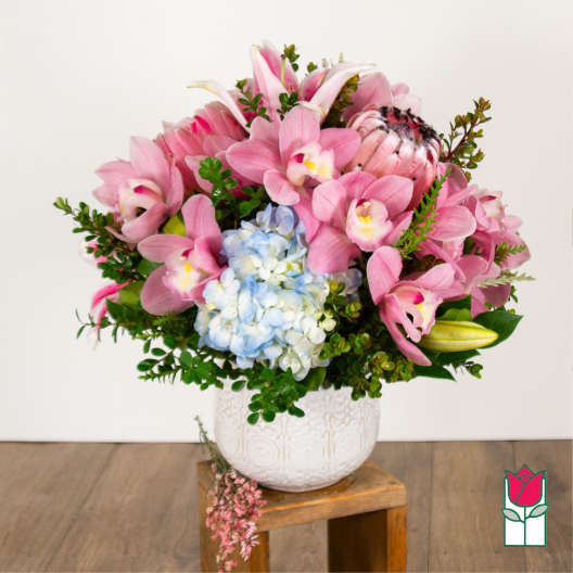 Pink orchid and lily arrangement with blue hydrangea in a white vase