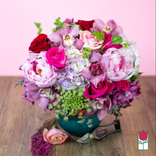 Pink and red floral arrangement in a teal vase on a wooden table