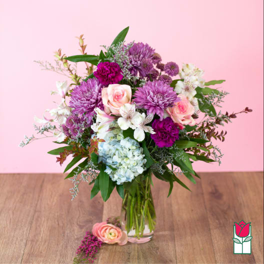 Mixed pink, purple, and white flower arrangement with hydrangea in a clear glass vase