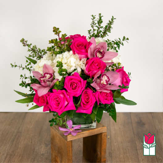 Bright pink roses, white hydrangeas, and pink orchids arranged in a clear glass vase.