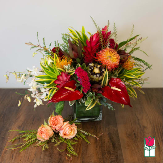 Tropical floral arrangement in a square glass vase with peach roses in front