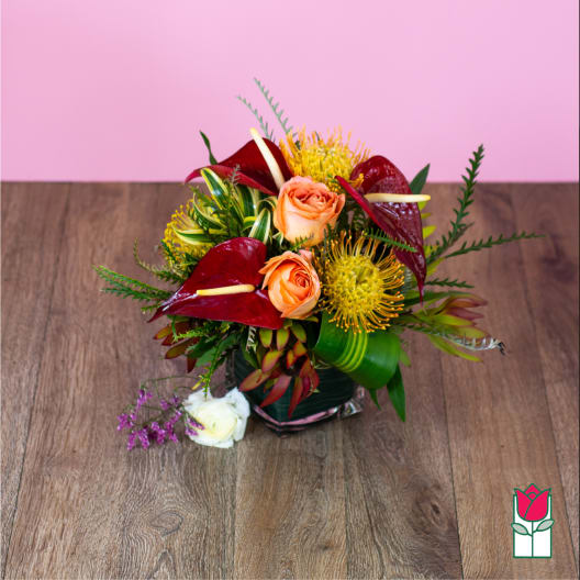 Tropical bouquet with peach roses and red anthuriums in a glass vase
